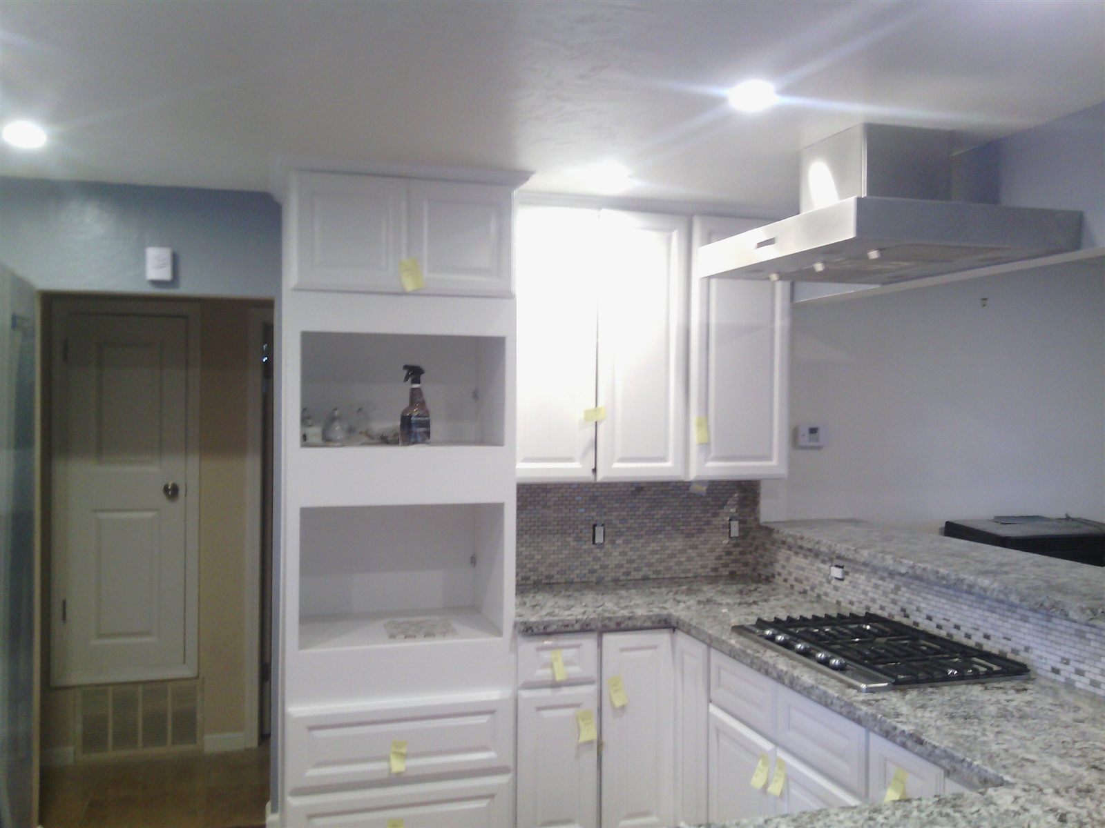 White kitchen cabinets, stone counters, tile backsplash, and stainless range hood